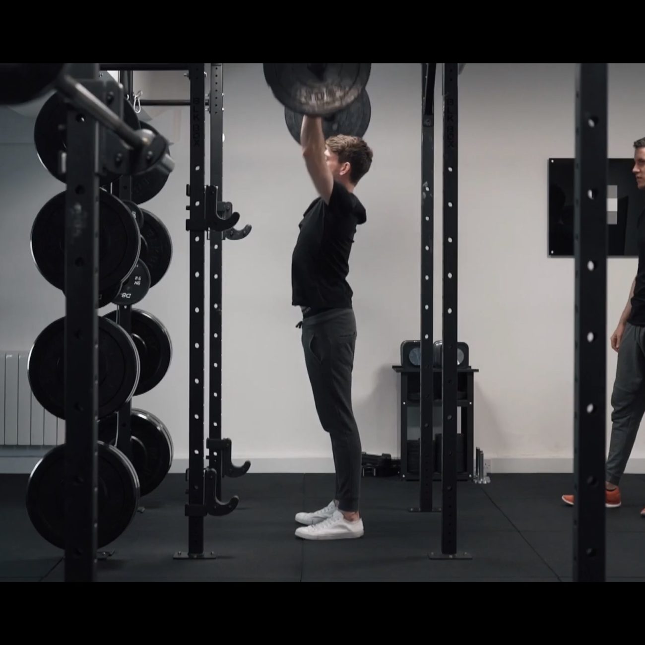 man pushing the barbell over head with the coach looking from back